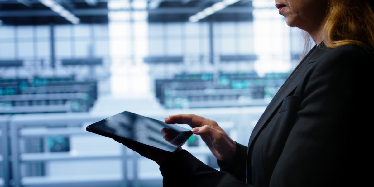 System administrator monitoring server room, doing checkup, inputting data on tablet of needed fixes. IT support employee working in data center facility housing storage rackmounts, camera B close up